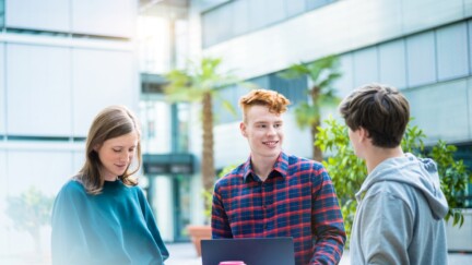 drei Studierende stehen vor einem Universitätsgebäude und unterhalten sich