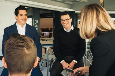 Drei Männer und eine Frau in Businesskleidung diskutieren miteinander und lächeln