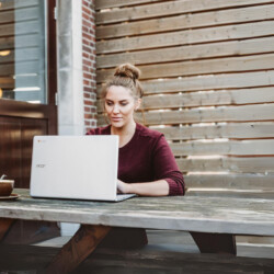 Frau sitzt und hält weißen Acer-Laptop in der Nähe einer braunen Holzwand