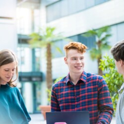 drei Studierende stehen vor einem Universitätsgebäude und unterhalten sich